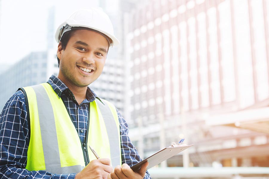 Business Insurance - Smiling Construction Worker Wearing a Hard Hat Takes Notes on a Clipboard